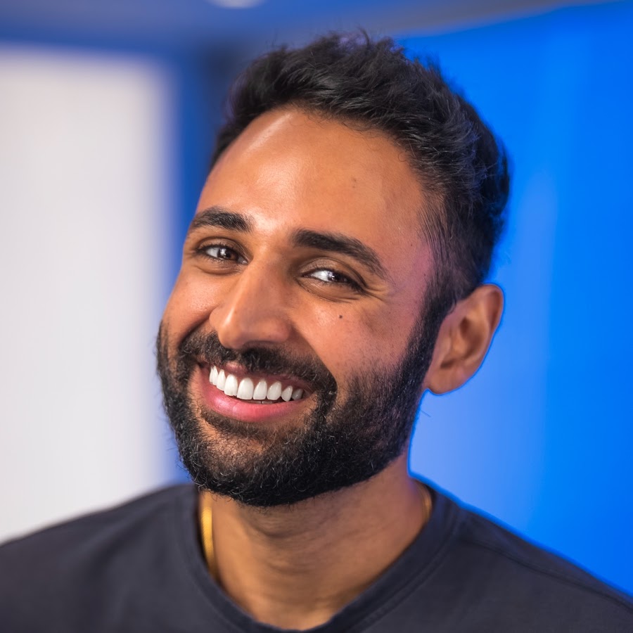 El avatar del canal Mrwhosetheboss: Arun Maini sonriendo, mirando fuera de cámara, contra una pared de estudio iluminada de azul